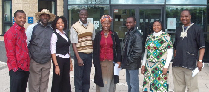 This images shows a group of eight African postgraduates standing in a line in front of a school entrance.