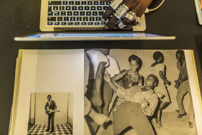 This photograph shows the keyboard of a lap top at the top of the image. There are photographs on the bottom half of the image. The smaller photo on the left is of a man standing playing a guitar. the larger photo on the right is of a group of men and women dancing.