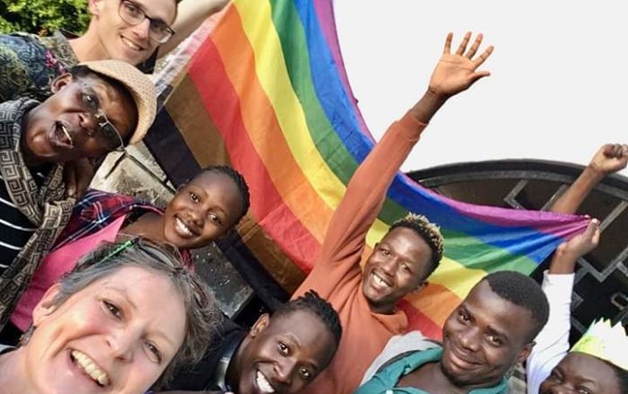 This image shows the two researchers, Adriaan van Klinken and Johanna Stiebert, with a group of the people they worked with on the project in front of a rainbow flag. 